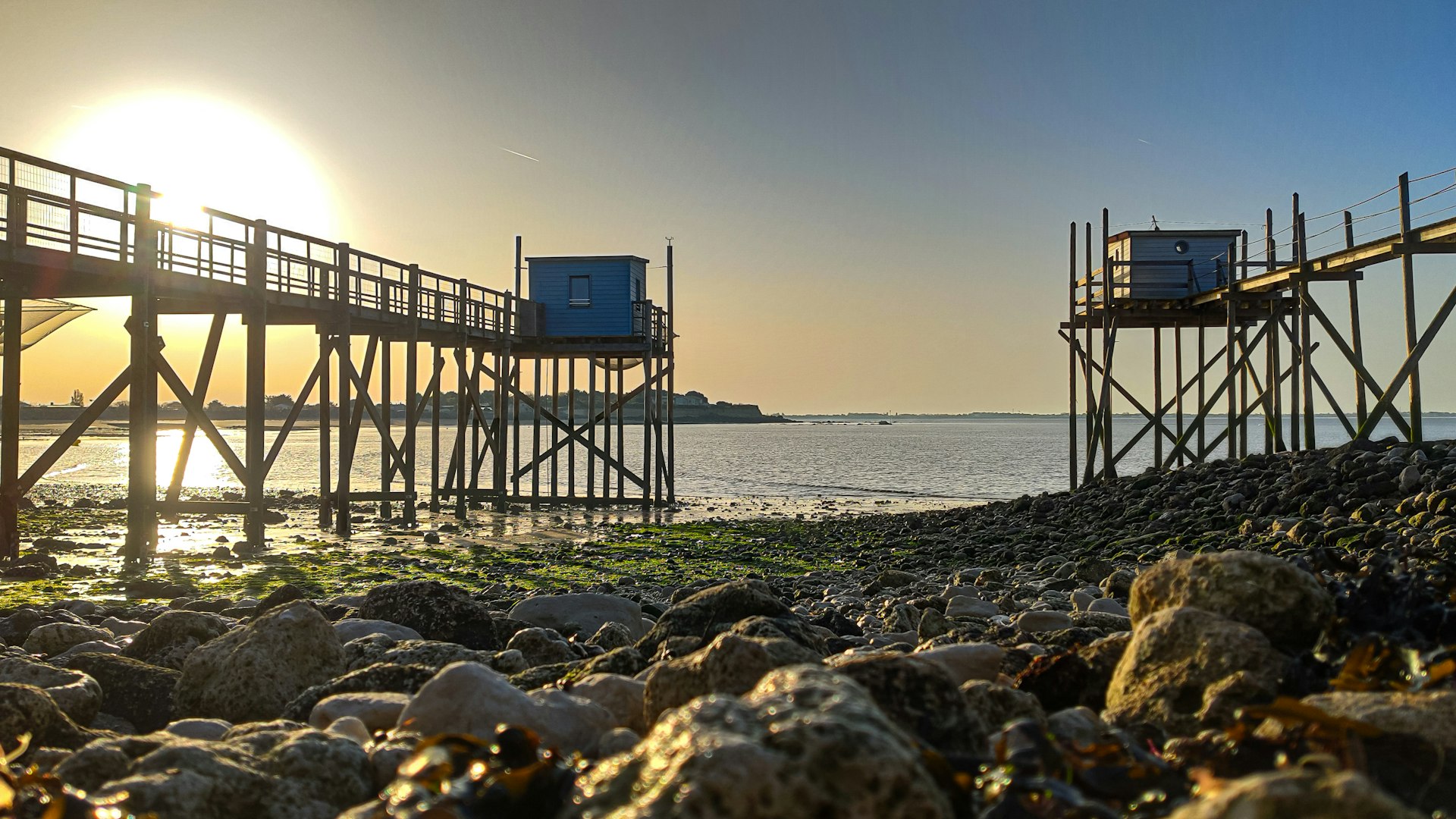 the sun is setting over the water near a pier
